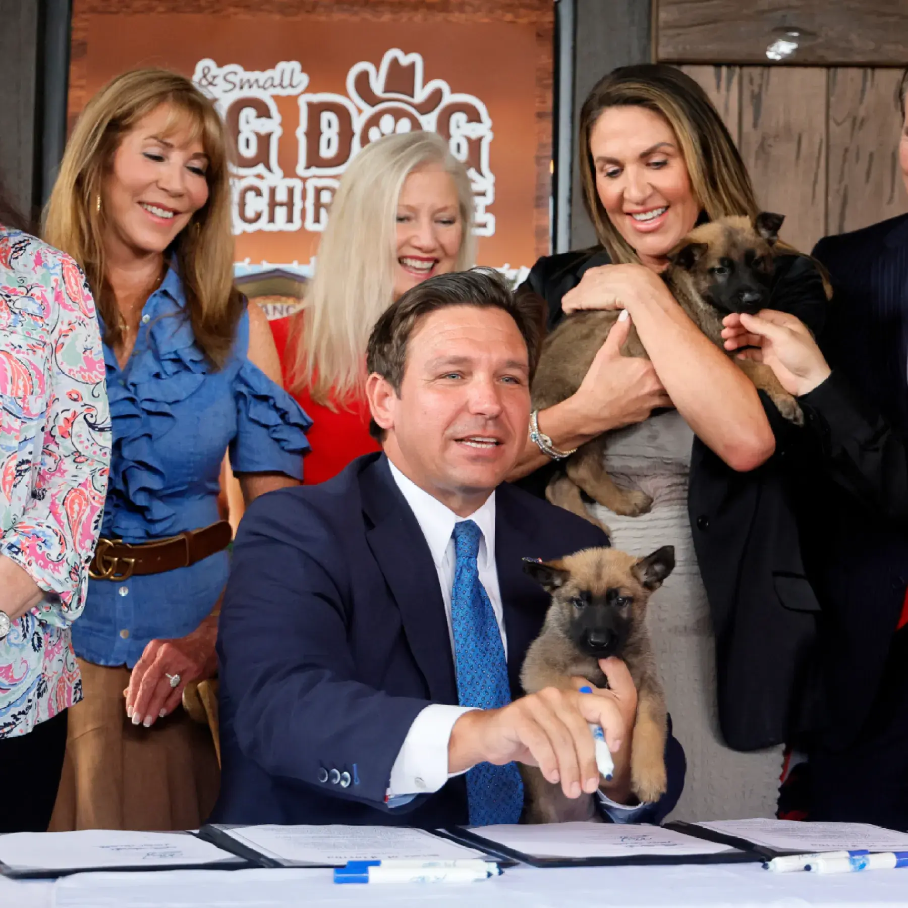 Governor Ron DeSantis signing animal welfare legislation while supporters hold rescued puppies